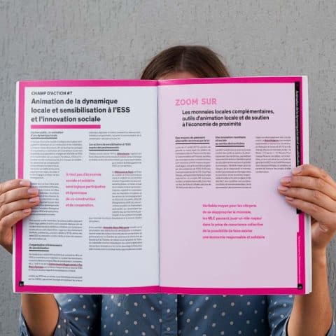 Une personne tient ouvert le livre de l'étude "Territoires Urbains" de l'Avise. Le contour de la double page est rose vif, la page de gauche est blanche et celle de droite rose pâle.